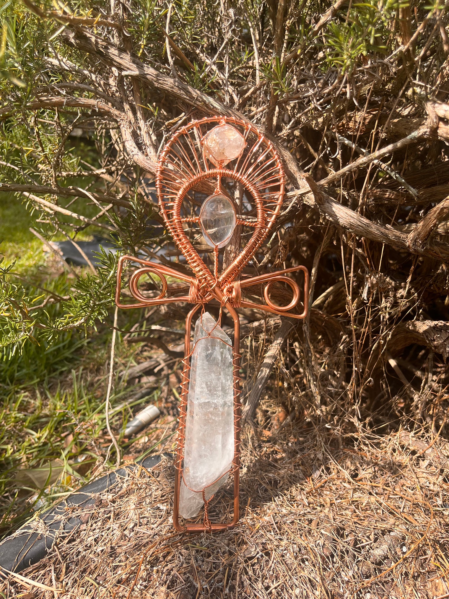 Hand holding a decorative cross with crystal stones against a natural background crystal quartz handle ankh with crystal gallet in the center and moroccan herkimer at the top