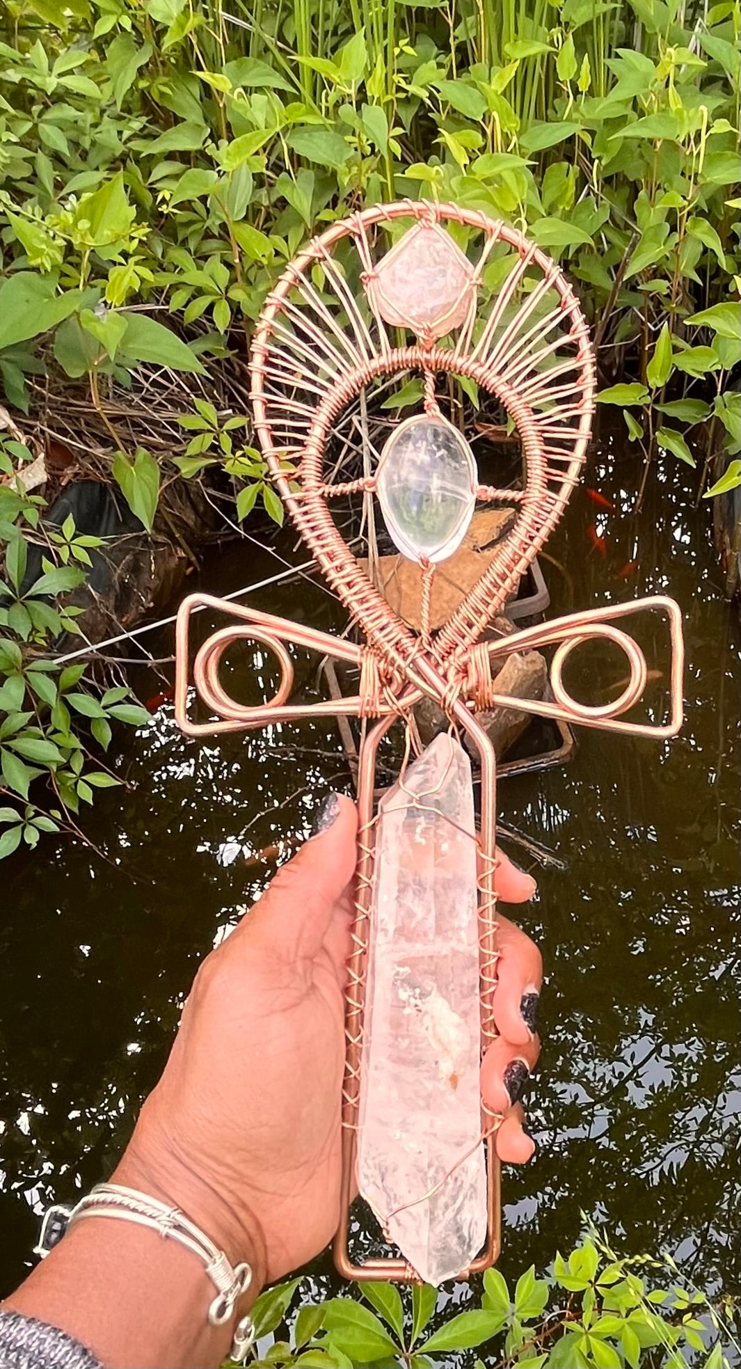 Hand holding a decorative cross with crystal stones against a natural background crystal quartz handle ankh with crystal gallet in the center and moroccan herkimer at the top