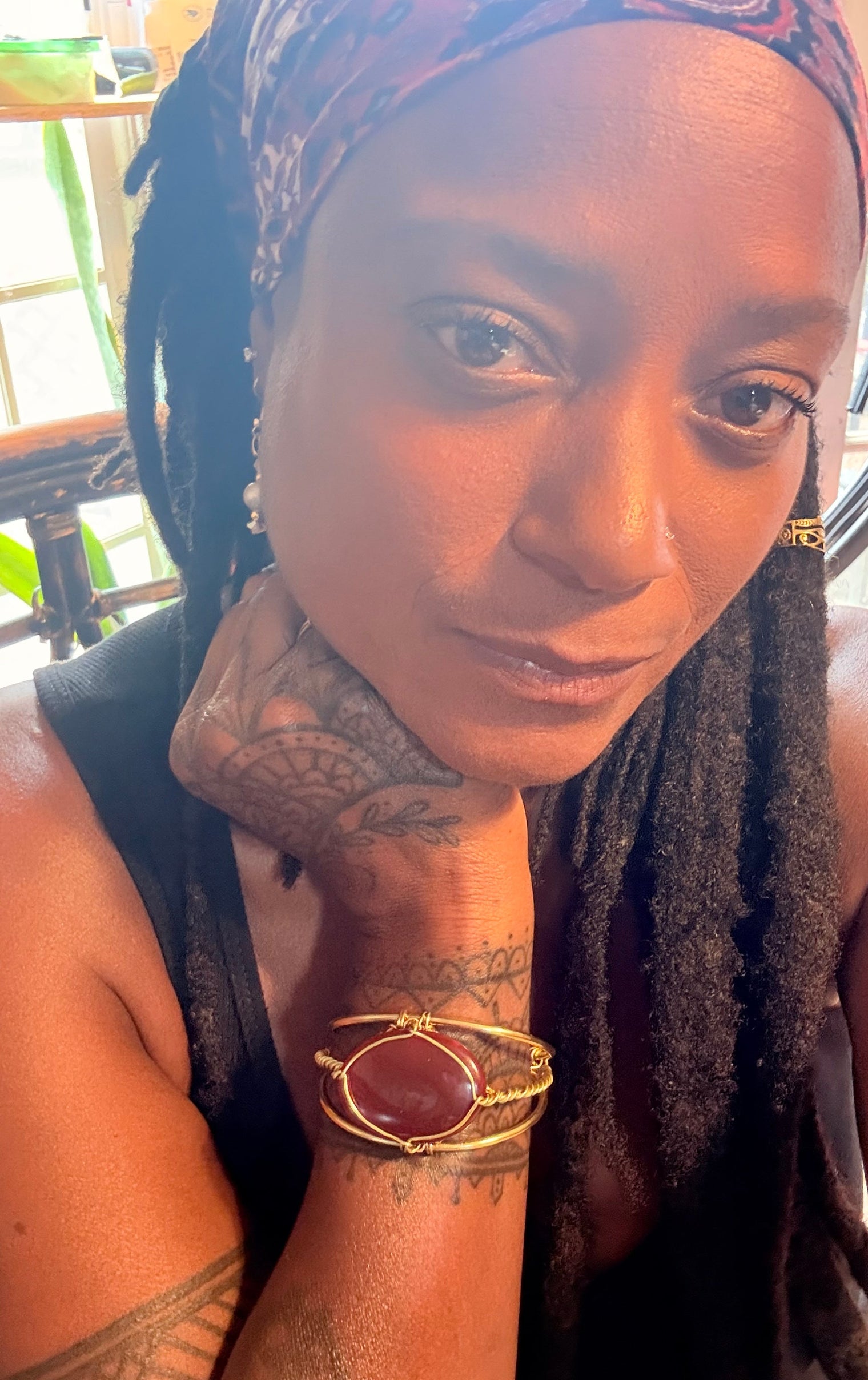Woman with long natural locs hair and tattoos wearing a headscarf indoors modeling carnelian brass wire wrapped bracelet