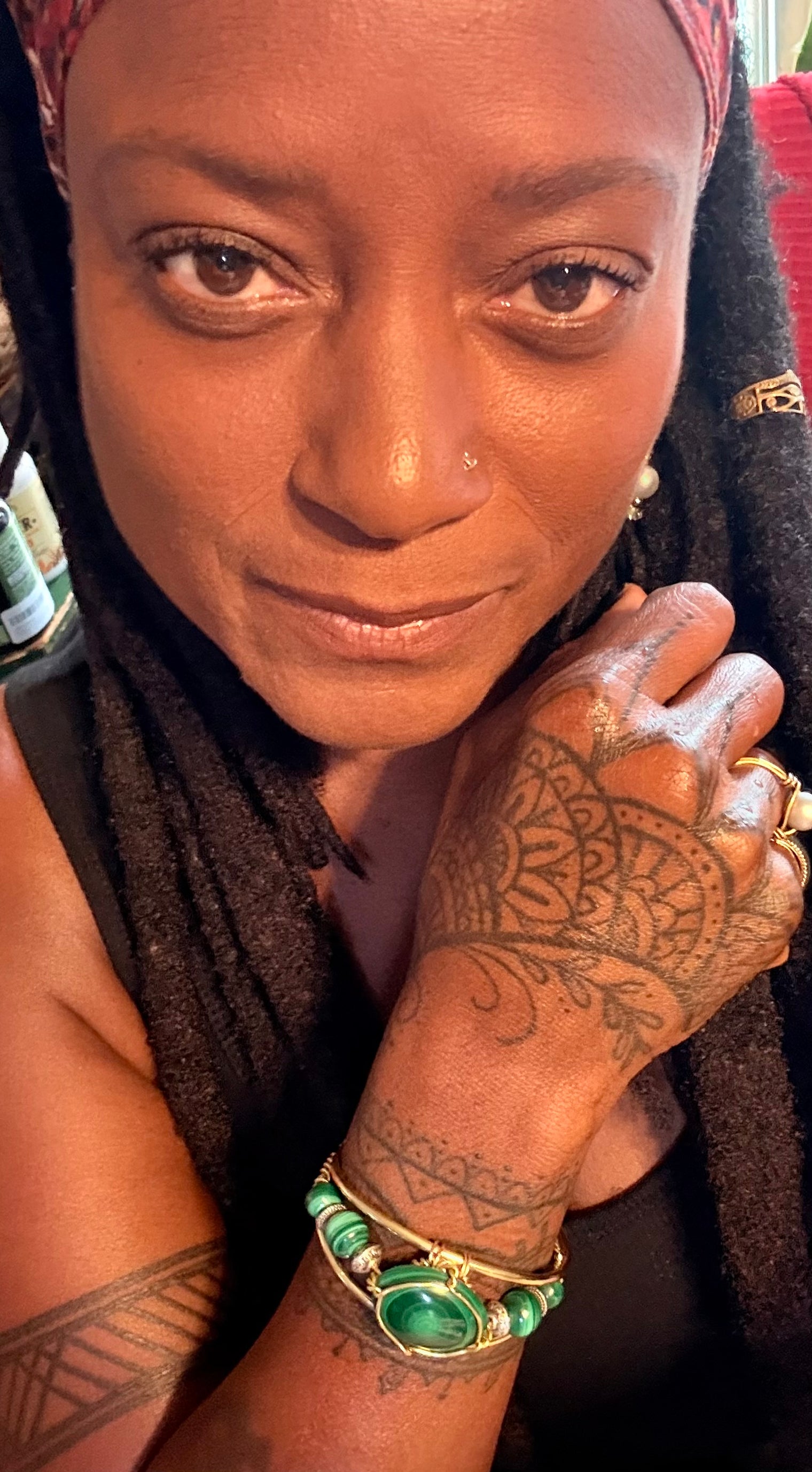 Person with tattoos and jewelry, including a green malachite wire wrapped bracelet and gold ring