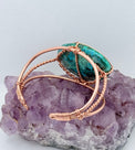 Jewelry with a green stone and rose gold wire wrapping on a purple crystal background the center stone of the copper bracelet is malachite chrysocolla 