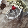 A silver wire bangle bracelet with a polished red jade gemstone accent, displayed on a cluster of smoky quartz crystals.
