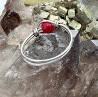 A silver wire bangle bracelet with a polished red jade gemstone accent, displayed on a cluster of smoky quartz crystals.