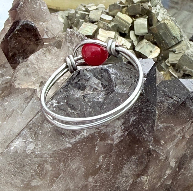 A silver wire bangle bracelet with a polished red jade gemstone accent, displayed on a cluster of smoky quartz crystals.