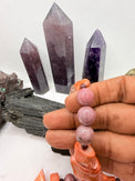 A pink and red coral coral bead necklace with chunky coral beads and small round garnet beads,rhodonite and pink opal and chocolate rhodocrosite  displayed on a white surface with crystal points and rocks in the background.